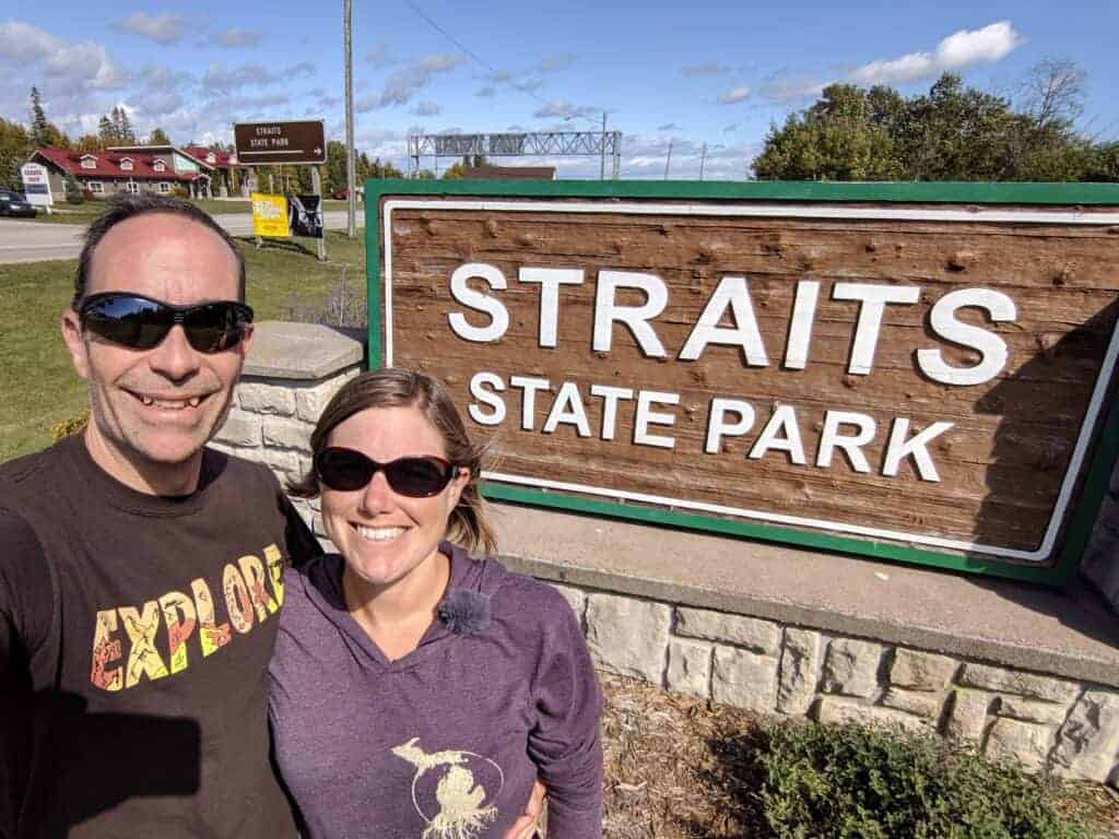 Two adults standing in front of the Straits State Park entrance sign
