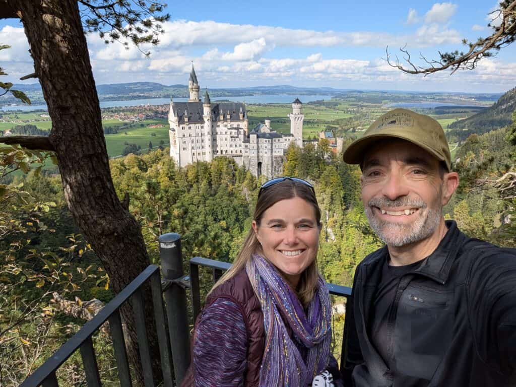 A couple enjoying a scenic view of Neuschwanstein Castle in Bavaria, Germany, during a hiking adventure with lush greenery and blue skies